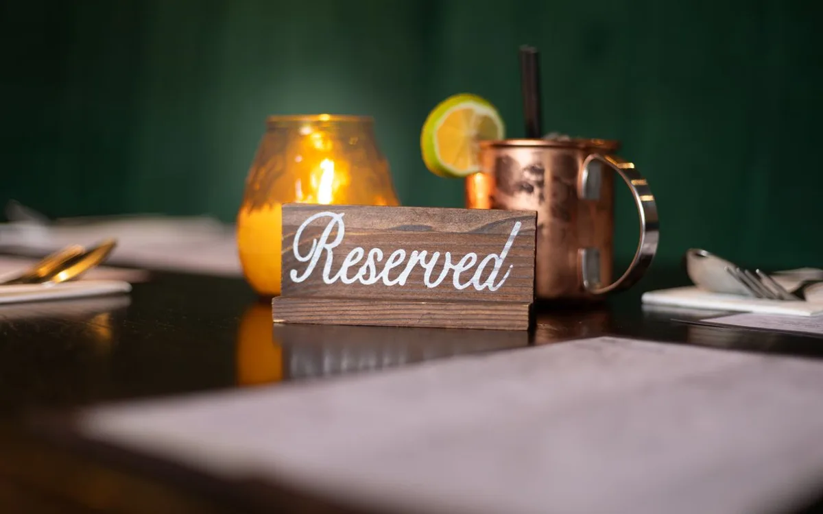 Cartel de madera con la palabra Reservado sobre una mesa de restaurante, con una vela y un trago